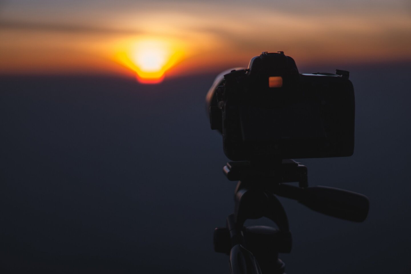 Das Foto zeigt eine Fotokamera auf einem Stativ vor einem Sonnenuntergang.
