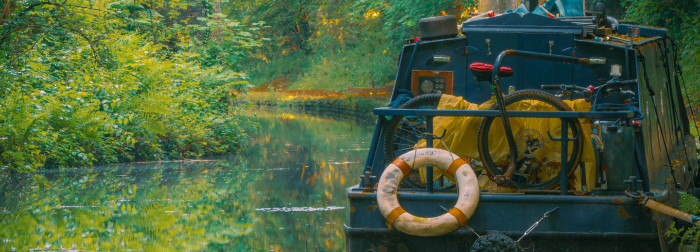 Ein Hausboot, das auf einem Fluss schwimmt. Im Hintergrund sind eine Brück eund Bäume zu sehen. 