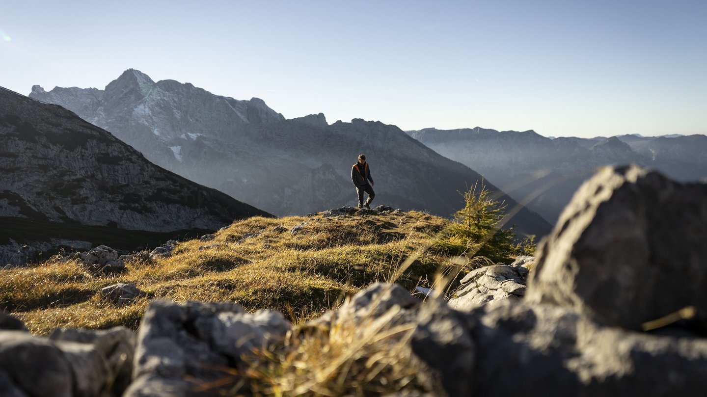 Das Foto zeigt eine Person, die in der Sonne auf einem Berg wandert.