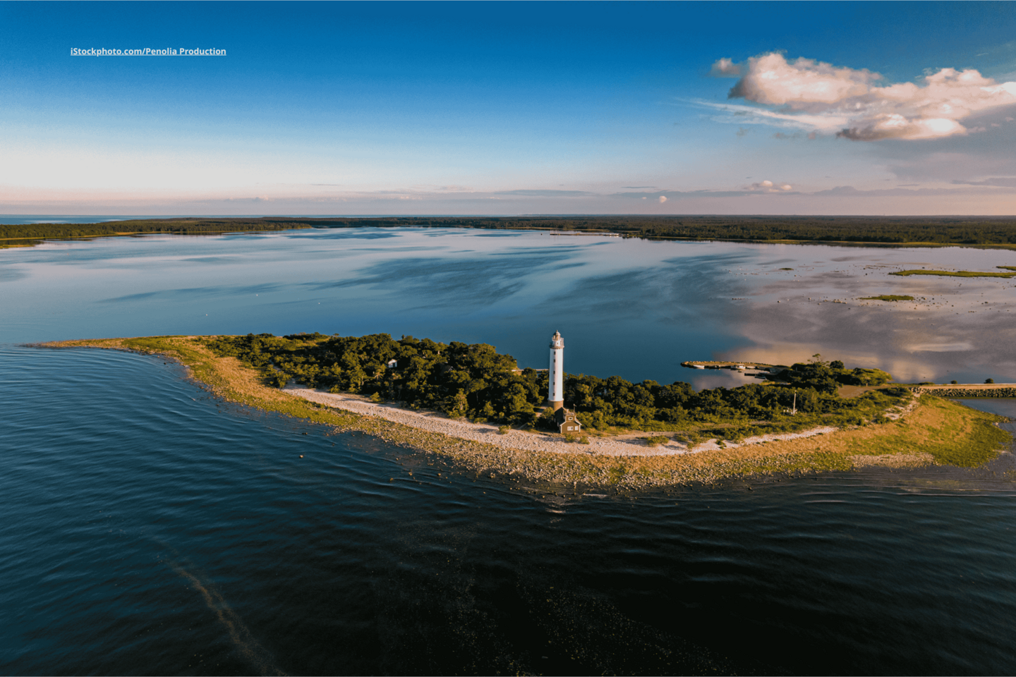 Eine Luftaufnahme vom Gipgel Ölands. Zu sehen sind blaues Meer und blauer Himmel, auf der Insel stehen viele grüne Bäume und ein großer, weißer Leuchtturm. 