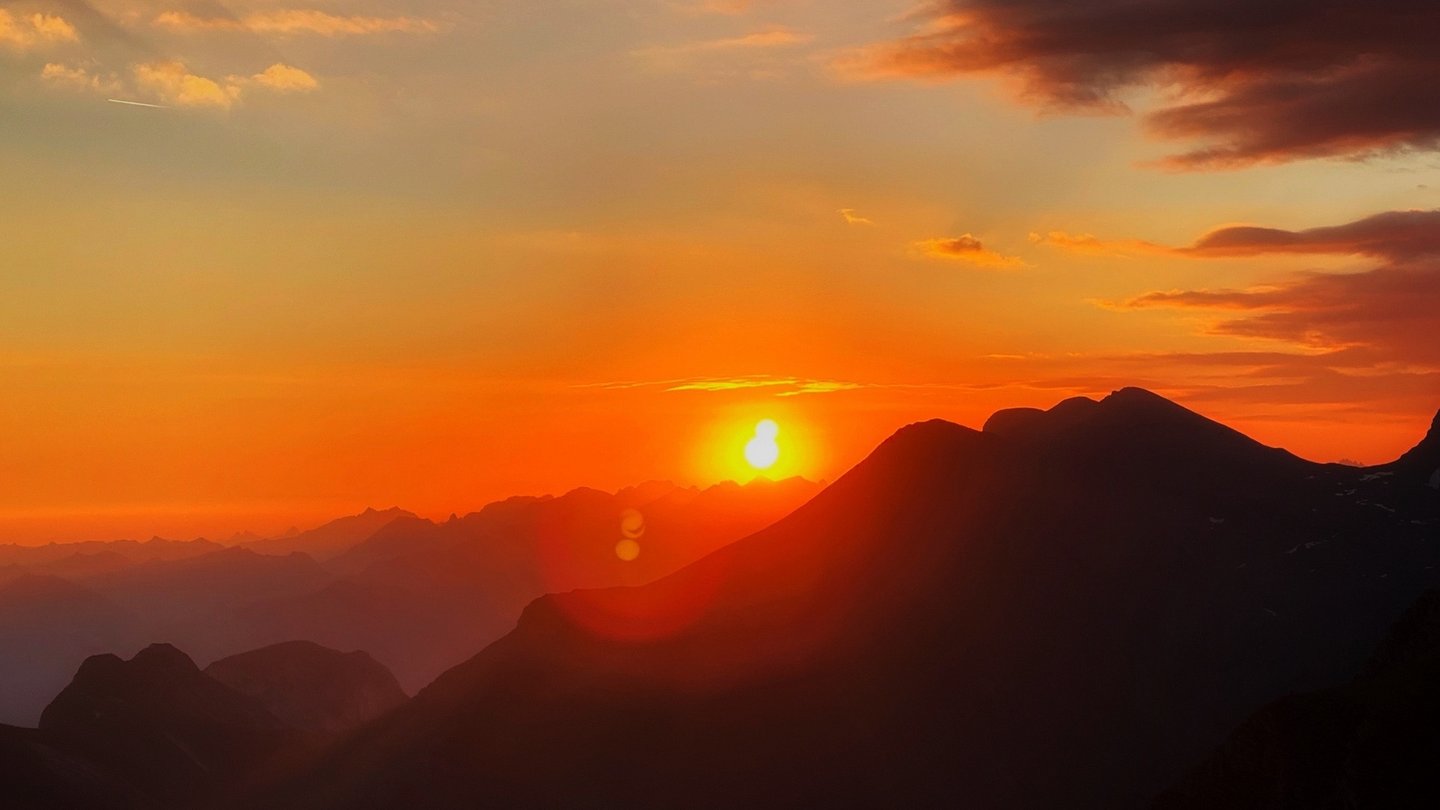 Das Bild zeigt einen roten Sonnenuntergang hinter Bergen.