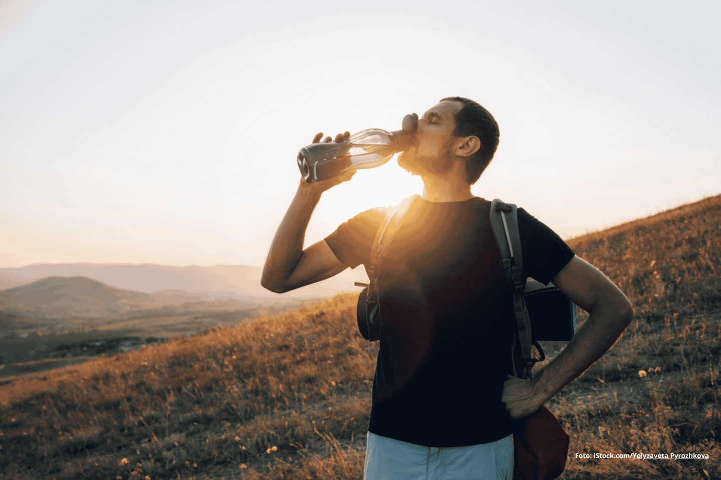 Das Foto zeigt einen Wanderer im Sonnenlicht, der Wasser aus einer Flasche trinkt.