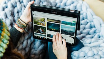 Frau mit Wollmütze sitzt auf der Couch und schaut auf einem Tablet Naturfotos auf Pinterest an.