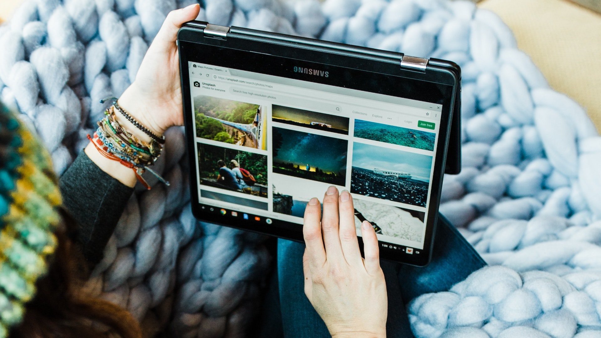 Frau mit Wollmütze sitzt auf der Couch und schaut auf einem Tablet Naturfotos auf Pinterest an.