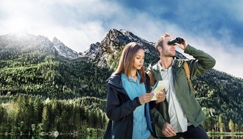 Das Foto zeigt zwei Personen in der Natur bei der Benutzung eines Fernglases.