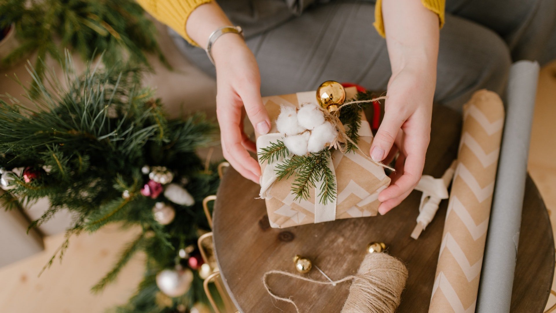 Das Foto zeigt die Hände einer Person, die ein Geschenk weihnachtlich verpackt.