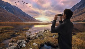 Das Foto zeigt einen Mann, der durch ein Fernglas Vögel bei Sonnenuntergang in der Natur beobachtet.