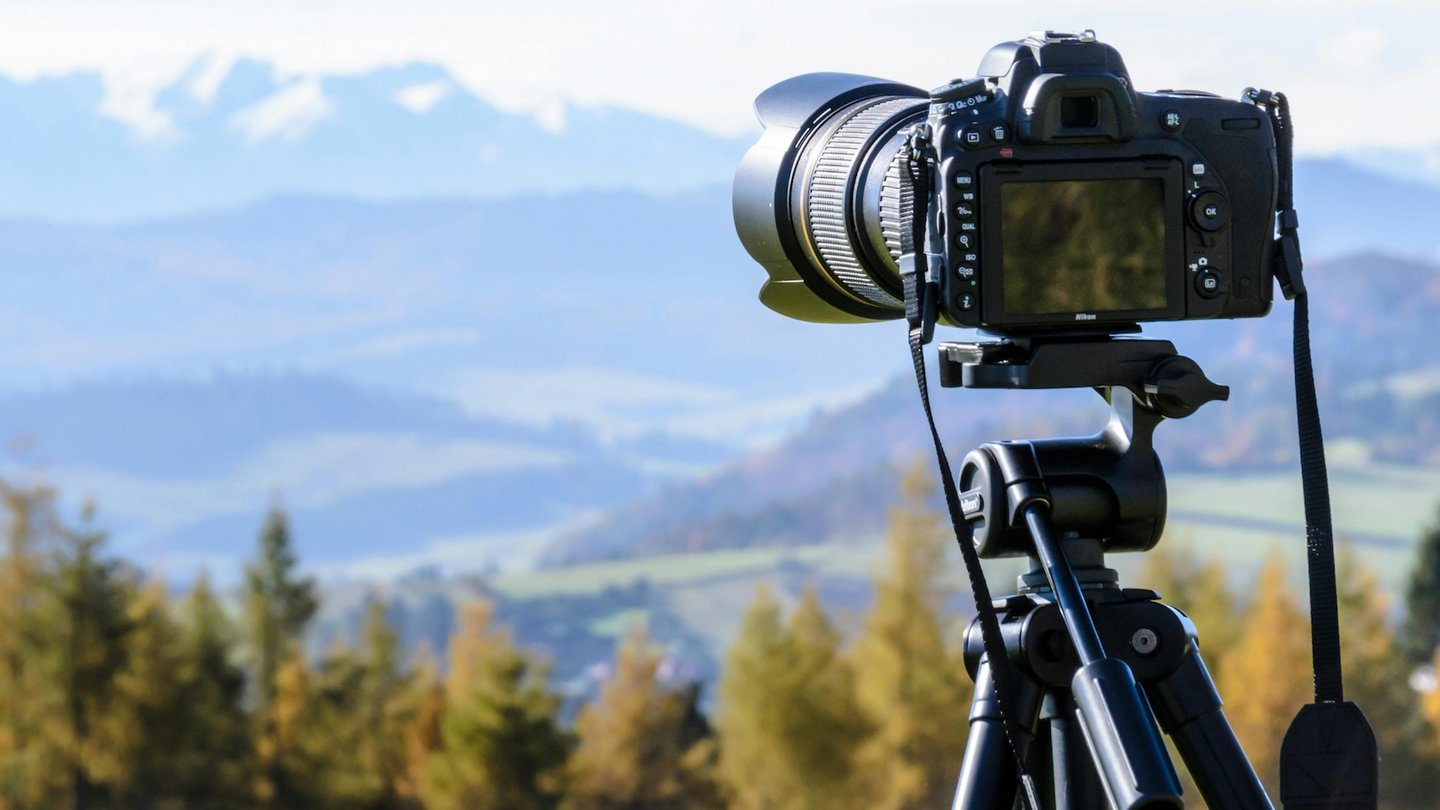 Das Foto zeigt eine Kamera auf einem Stativ vor grüner Berglandschaft.