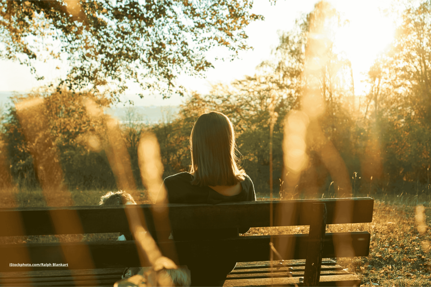 Das Foto zeigt eine Frau auf einer Parkbank sitzend bei Sonnenuntergang.
