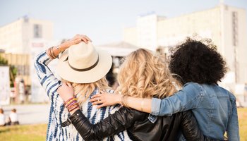 Das Bild zeigt drei Frauen, welche Arm in Arm vor einer Freilichtbühne stehen.