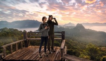 Das Foto zeigt zwei Personen auf einer Berglandschaft mit Ferngläsern.