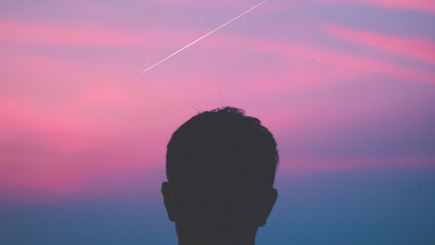 Mensch vor pinkem Sonnenuntergangshimmel mit einer Sternschnuppe.