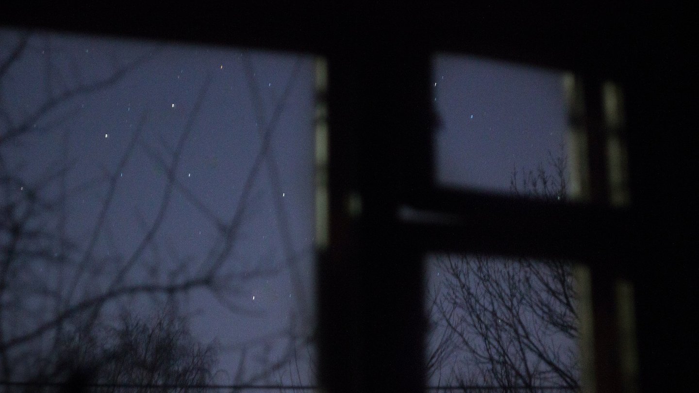Das Foto zeigt den blauen Sternenhimmel hinter einem verschwommenem Fensterrahmen.