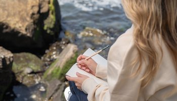 Das Foto zeigt eine Frau, die in der Natur Journaling betreibt.