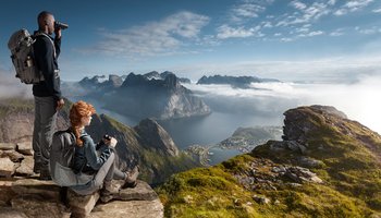 Bild von zwei Personen die mit Ferngläser auf eine Berglandschaft schauen.