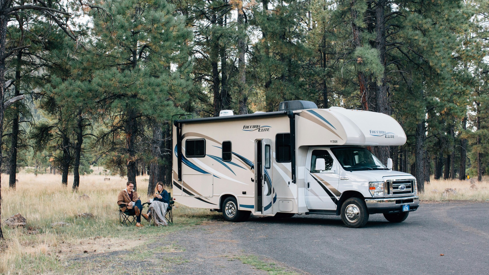 Das Foto zeigt zwei Personen vor einem Camper in der Natur.