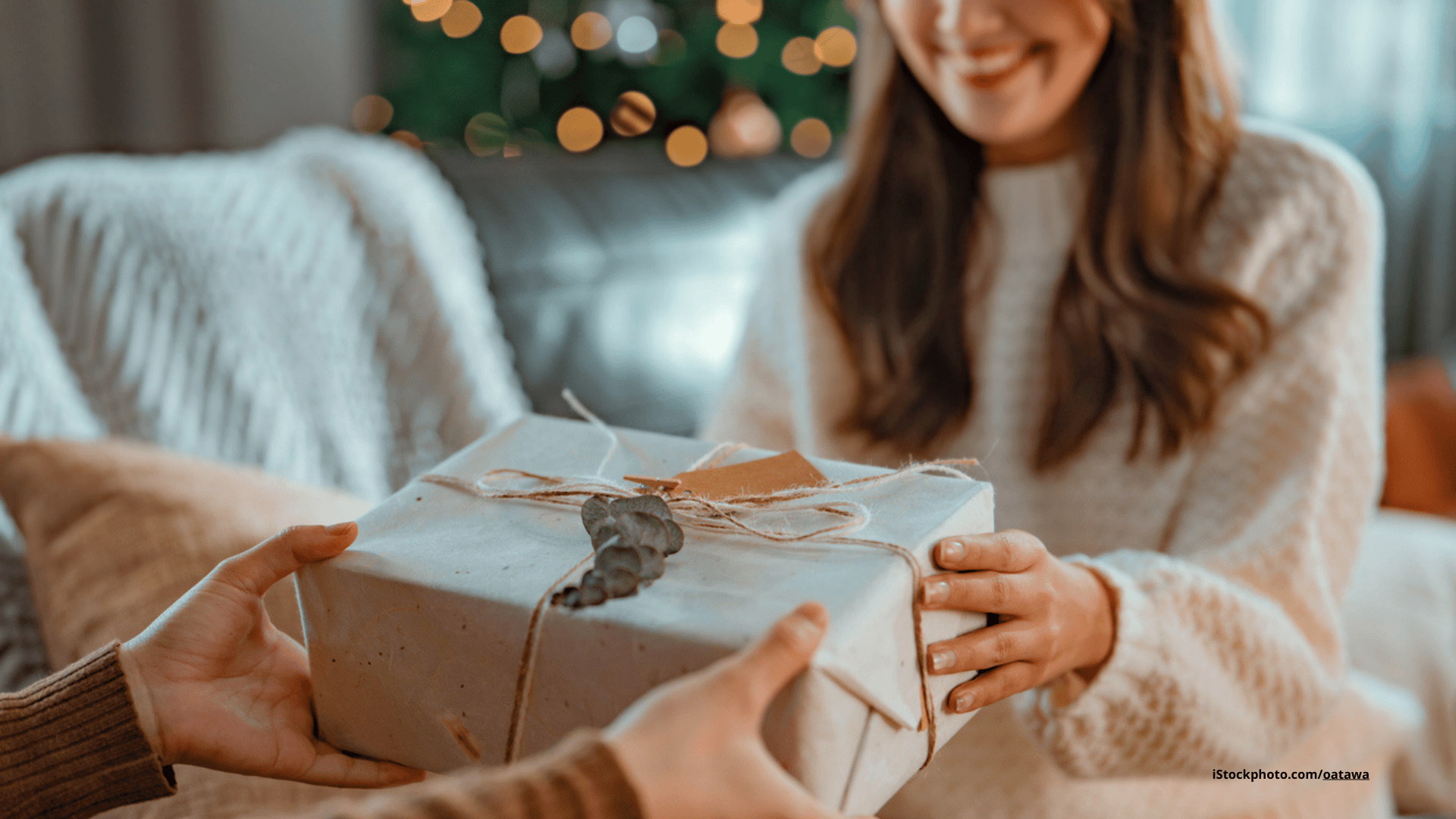 Das Foto zeigt eine Frau, die vor dem Weihnachtsbau ein Geschenk überreicht bekommt.
