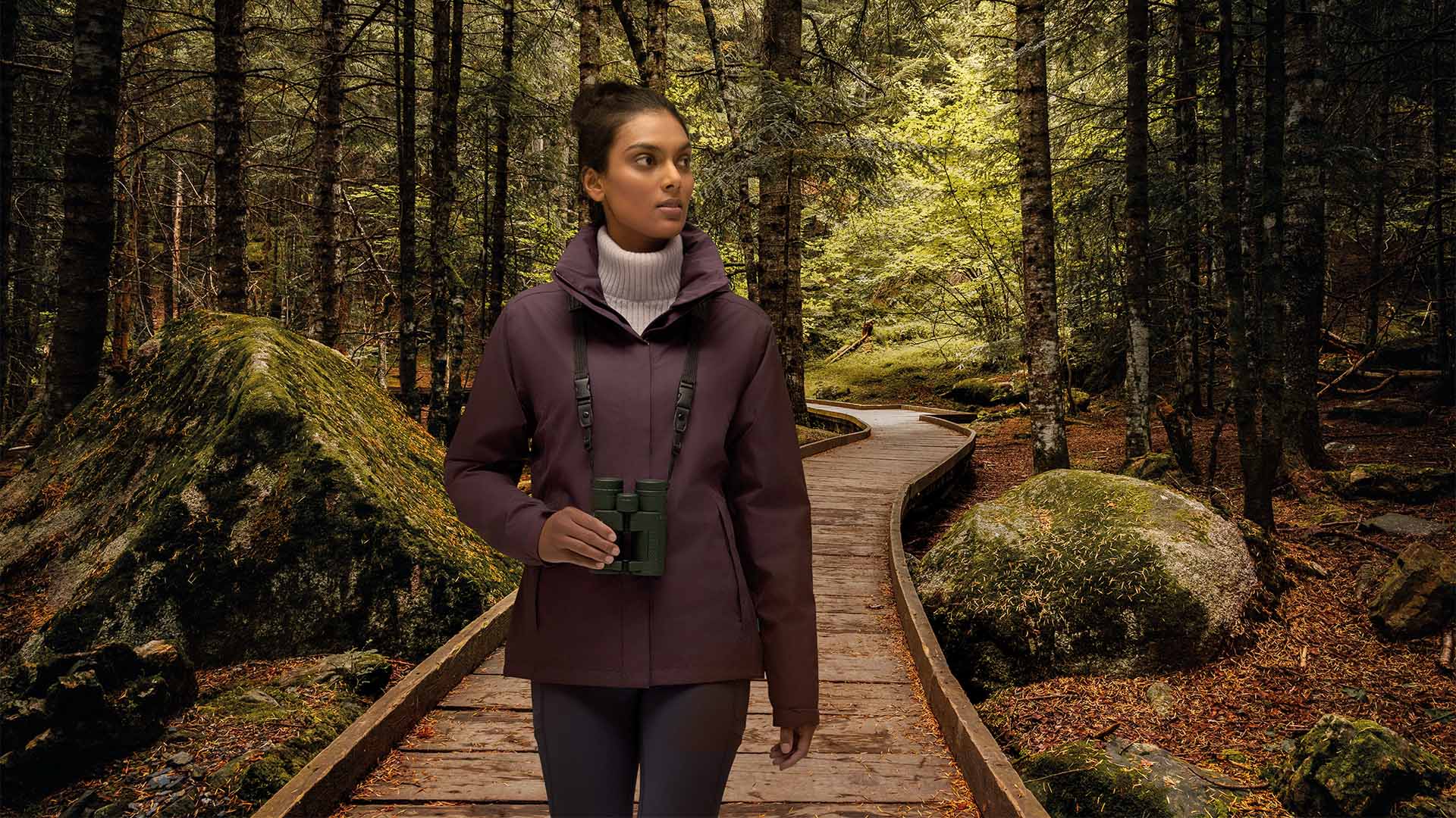Das Foto zeigt eine Frau mit Fernglas auf einem Spaziergang im Wald. 